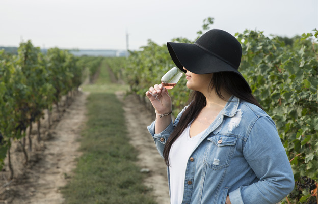 Girl in black hat holding wine glass in vineyard