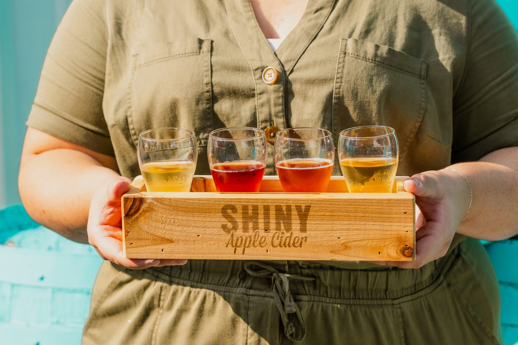 Person holding flight of 4 glasses of Shiny Apple Cider